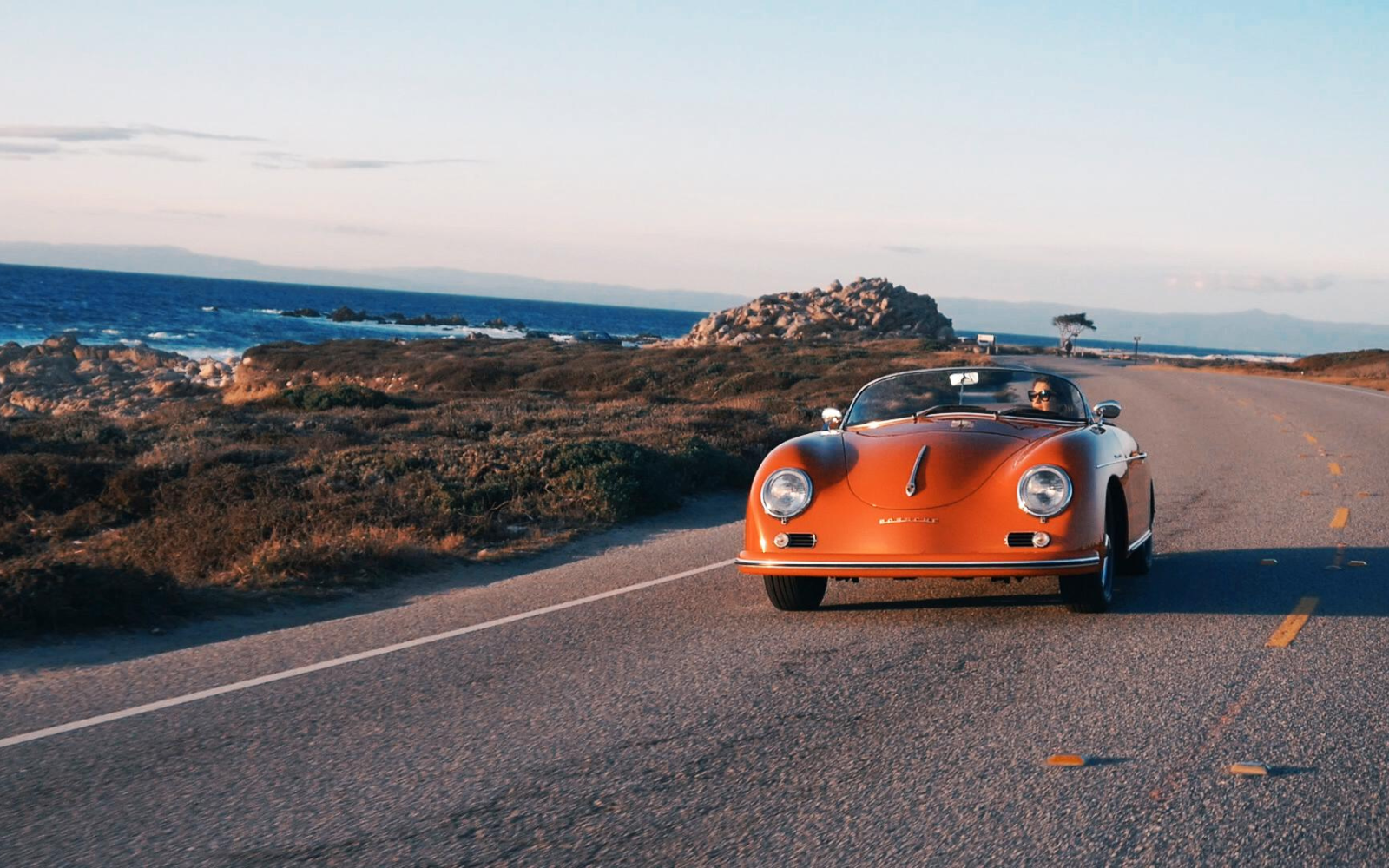 person driving down the california coast in a red classic porsche